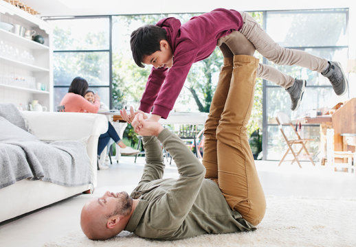 Father lifting son with legs on living room floor