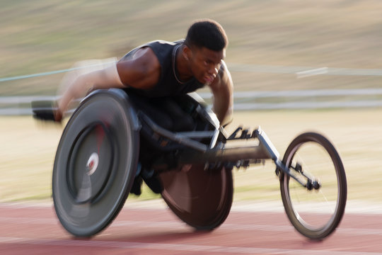 Determined young male paraplegic athlete speeding along sports track in wheelchair race