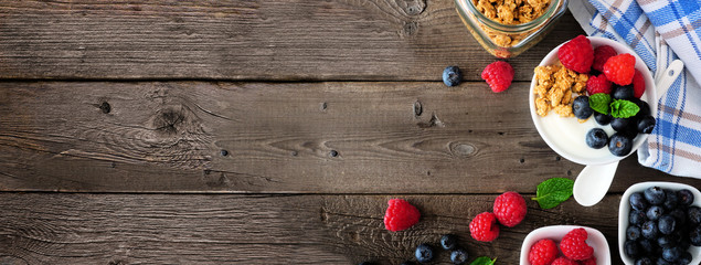 Healthy yogurt with fresh berries and granola. Banner with side border against a rustic wood background. Copy space.