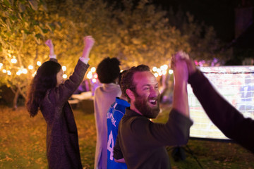 Happy friends cheering, watching sports in backyard