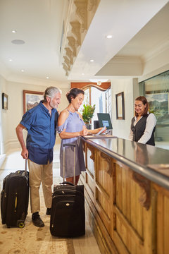 Mature Couple With Suitcases Checking In At Hotel Reception