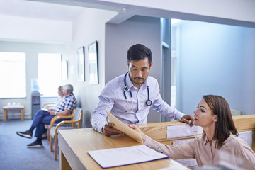 Doctor and receptionist discussing medical chart at clinic reception