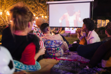 Friends watching movie on projection screen in backyard