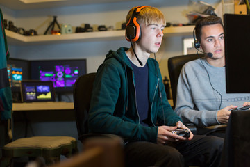 Teenage boys with headphones playing video game at computer in dark room