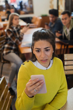 Worried young woman using smart phone in cafe