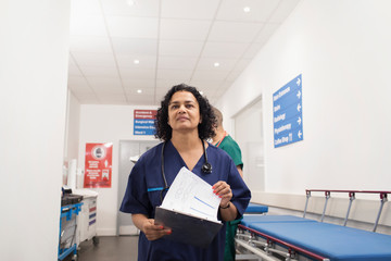 Confident female doctor with medical chart making rounds in hospital corridor