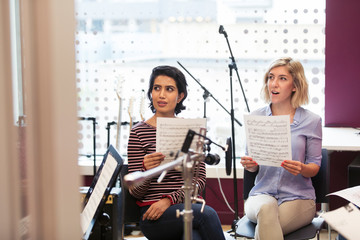 Women with sheet music singing in music recording studio