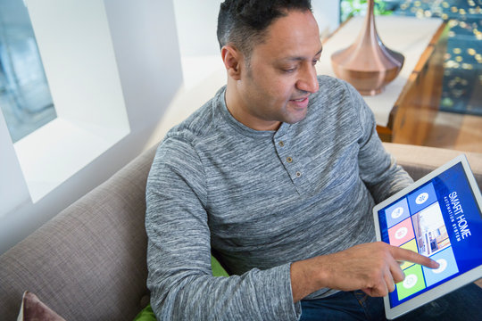 Man setting smart home alarm from digital tablet on living room sofa