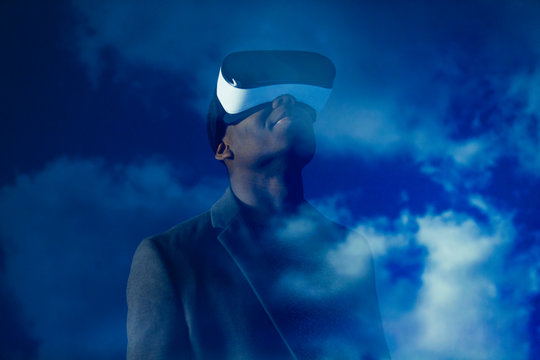 Double exposure businessman with virtual reality simulator glasses against blue sky with clouds