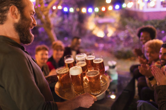 Man serving tray of beers to friends at garden party