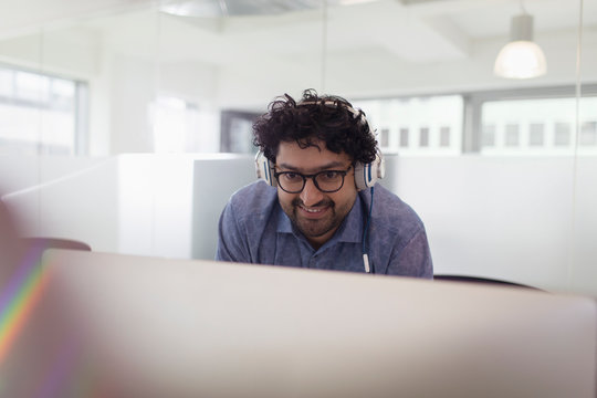 Smiling Businessman With Headphones Working At Computer In Office