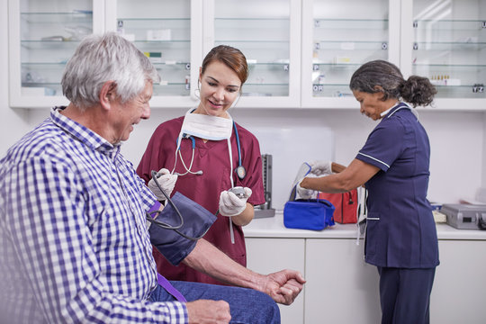 Female nurse checking blood pressure of senior male patient in clinic examination room
