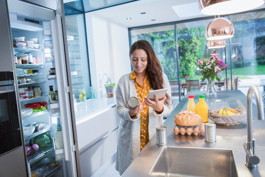 Woman with digital tablet checking food labels in kitchen
