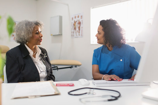 Female doctor talking with senior patient at computer in doctors office