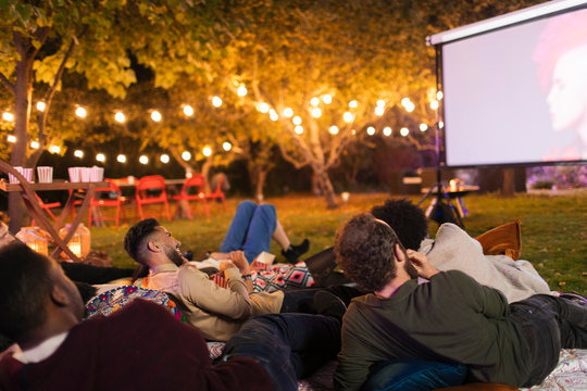 Friends relaxing, watching movie on projection screen in backyard