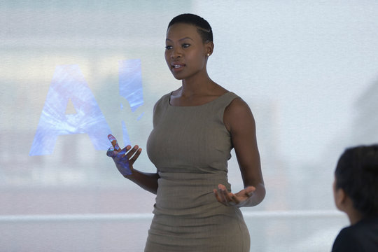Businesswoman leading meeting at projection screen with AI text