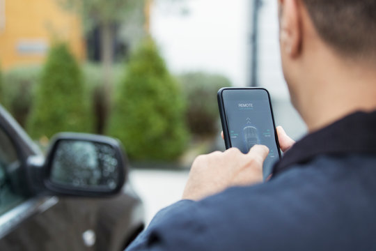 Man setting car alarm from smart phone in driveway
