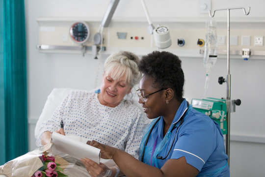 Female nurse discussing paperwork with senior patient in hospital room