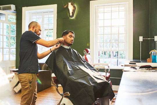 Male barber giving customer a haircut in barbershop