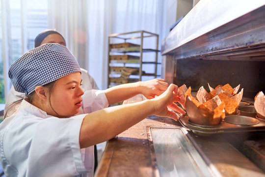 Young woman with Down Syndrome placing muffins in oven