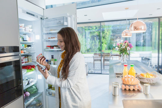 Woman with digital tablet at refrigerator in kitchen