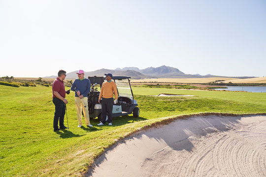 Male golfer friends talking at sand trap on sunny golf course