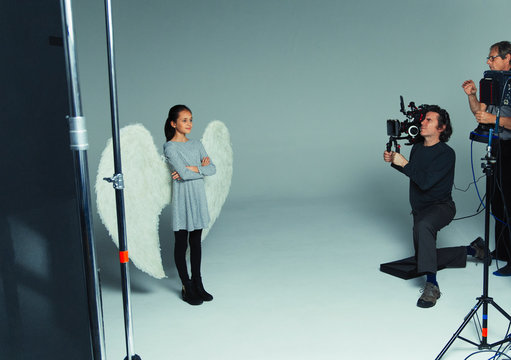 Girl in angel wings posing for photographers during photo shoot in studio