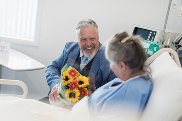 Happy senior man with flower bouquet visiting wife in hospital
