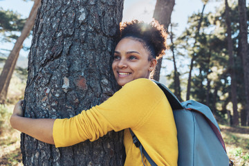Happy, carefree young female hiker hugging tree in sunny woods