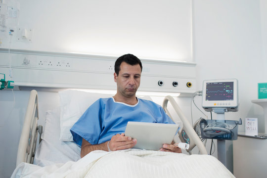 Male patient using digital tablet, resting in hospital bed