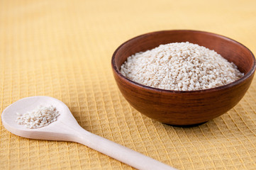 White sesame seeds in a clay Cup and wooden spoon on the table