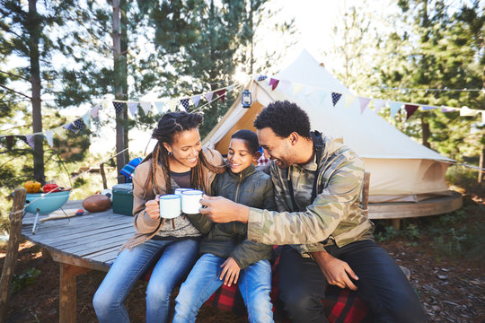 Happy family drinking coffee and hot chocolate at campsite in woods