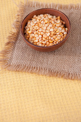 Pea groats in a clay Cup on a burlap table, top view