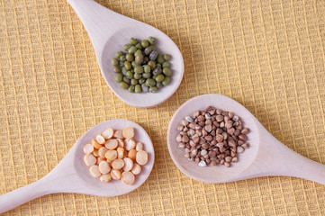 Three wooden spoons with buckwheat, mash and peas on the table, top view