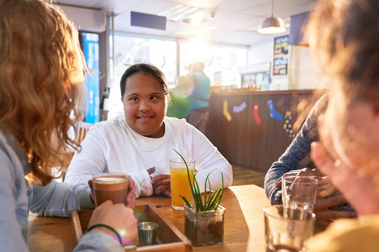 Smiling young woman with Down Syndrome talking with friends in cafe