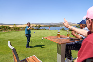 Male golfer friends drinking beer and practicing putting