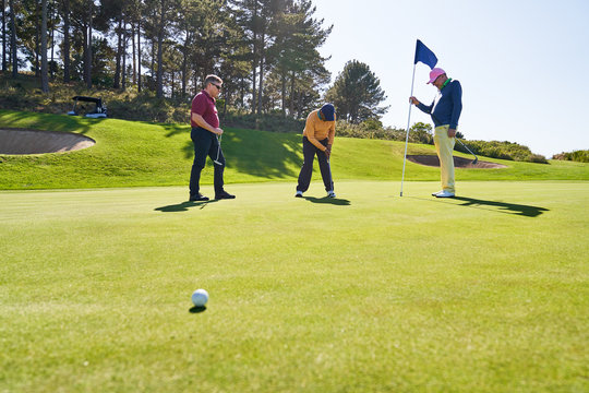 Male Golfer Friends Putting At Home On Sunny Golf Course