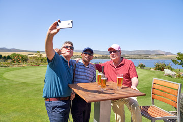 Male friends drinking beer and taking selfie on golf course patio