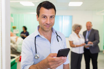 Portrait confident male doctor using smart phone in hospital ward