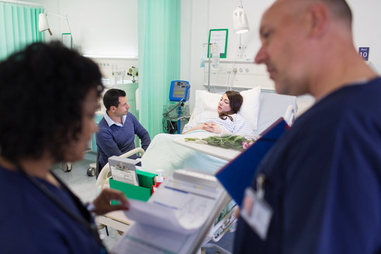 Doctors with medical chart making rounds with patient resting in hospital bed in background