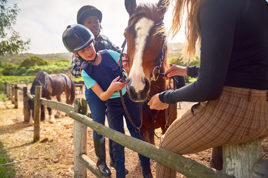 Woman and girls preparing horse for horseback riding in paddock