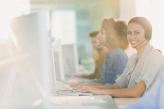 Portrait smiling businesswoman with headset working at computer in office