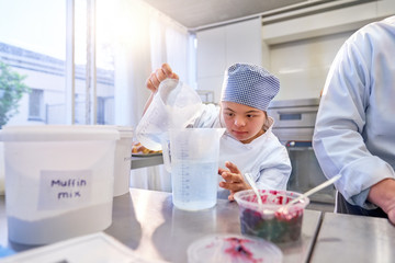 Focused young female student with Down Syndrome baking in kitchen