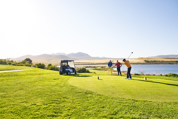 Male golfer teeing off at sunny lakeside tee box