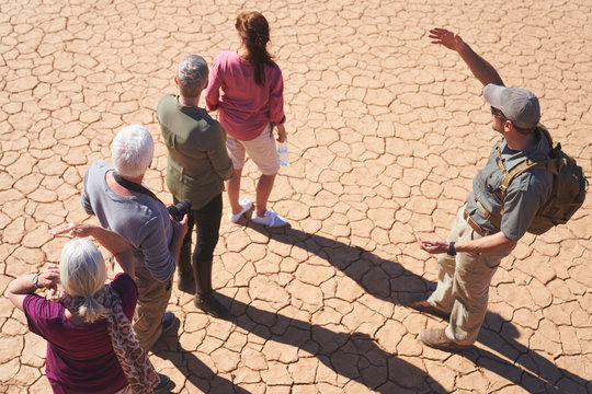 Safari tour guide talking with group on sunny cracked earth