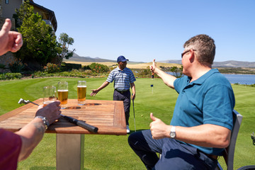 Male golfers drinking beer cheering friend on practice putting green