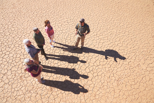 Safari tour guide talking with group on sunny cracked earth