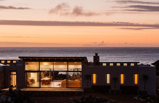 Illuminated luxury home overlooking ocean at sunset
