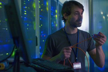Server room technician examining cable at computer
