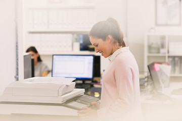 Smiling businesswoman making copies at copier in office